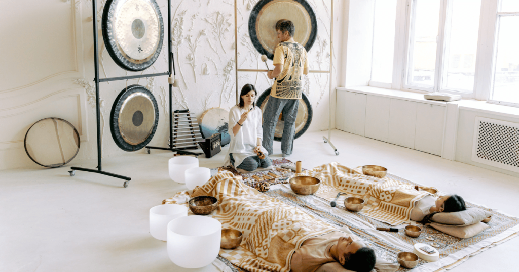 two people experience sound therapy using gongs, singing bowls and various container and bells.