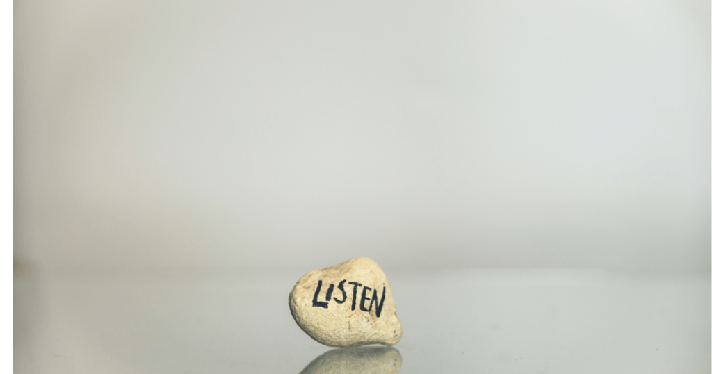 a beige stone with the word 'Listen' written on it sits on a polished surface in a wide neutral space